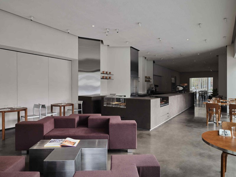 Open cafe interior showing kitchen counter, purple upholstered seating, and polished concrete floor under a white ceiling