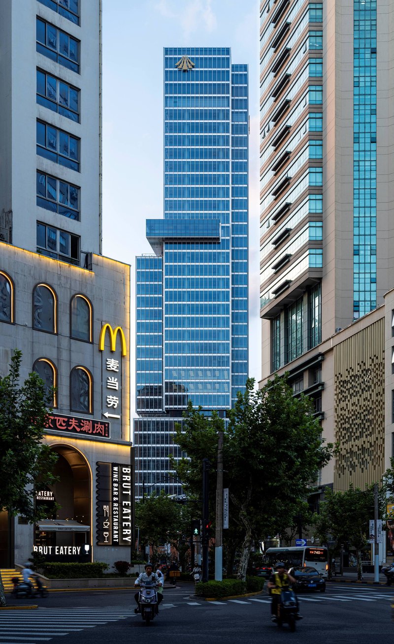Street view of the glass tower rising between neighboring buildings with motorcycles passing at dusk