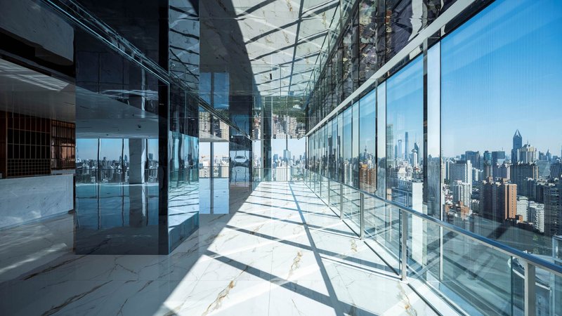Glass-enclosed corridor with white marble floor and cityscape views under bright sunlight