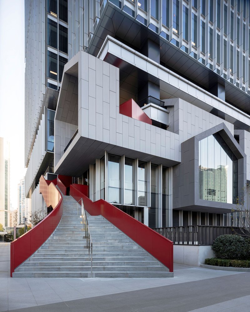 Concrete stair with red sculptural railings leading up to the white panel and glass tower entrance