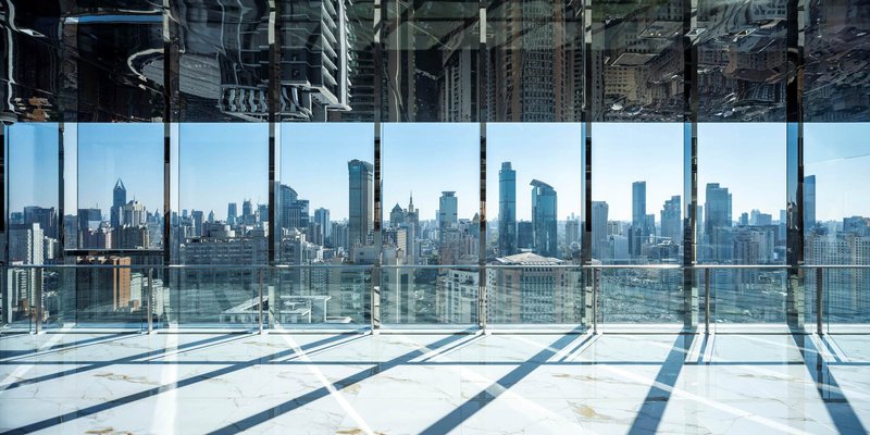 Floor-to-ceiling glass wall framing the skyline with strong sunlight casting mullion shadows across the polished floor