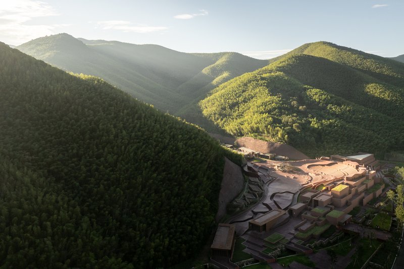 Aerial view of the complex nestled into a valley with surrounding forested mountains at dusk