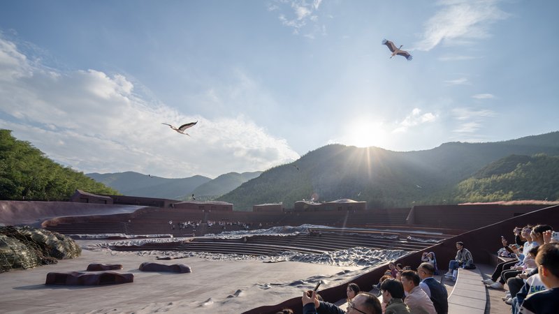 Performance space with spectators watching as raptors circle above the mountain valley below