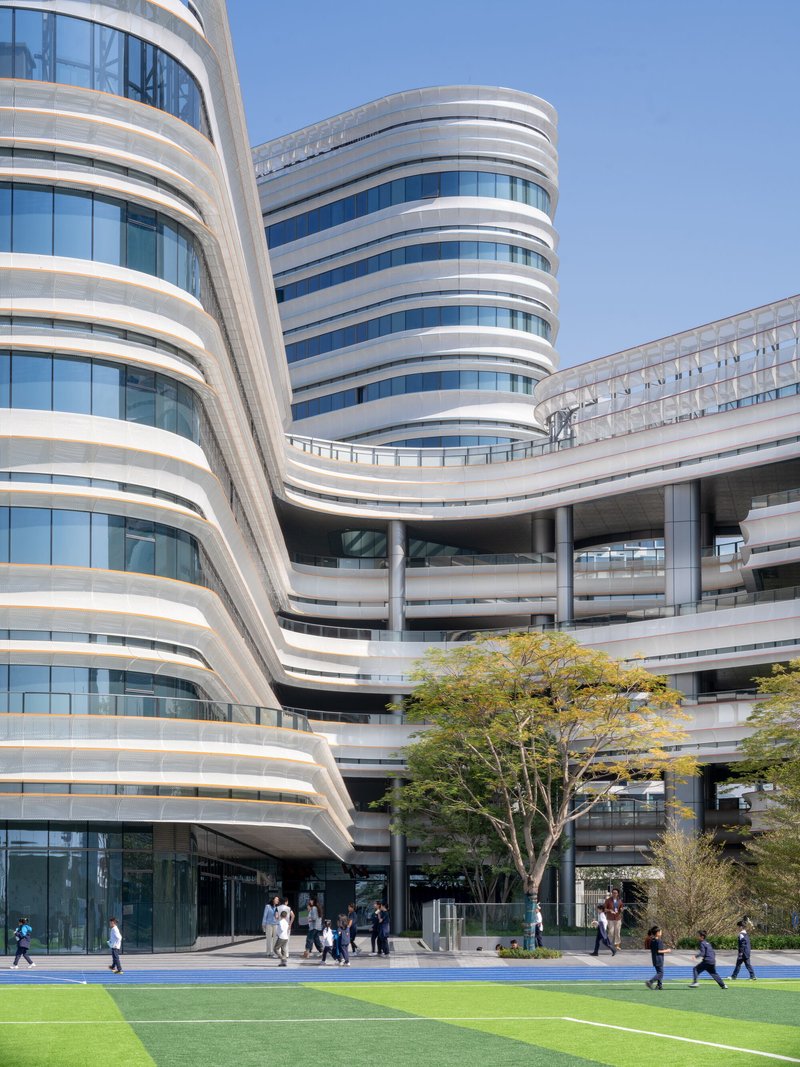 Ground-level view of curved facade towers with alternating white bands and glazing above blue track and green lawn