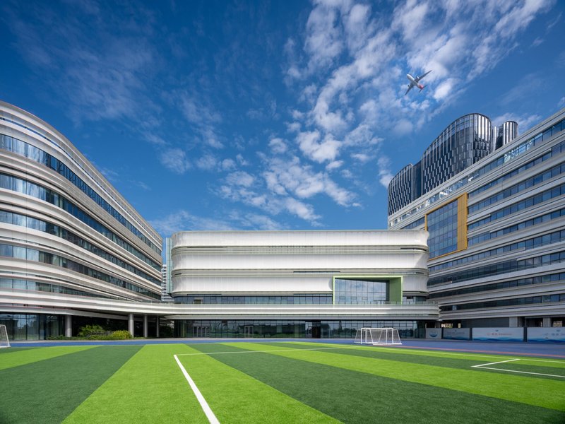 Courtyard view of the rounded white volume and flanking facades with an airplane crossing the blue sky