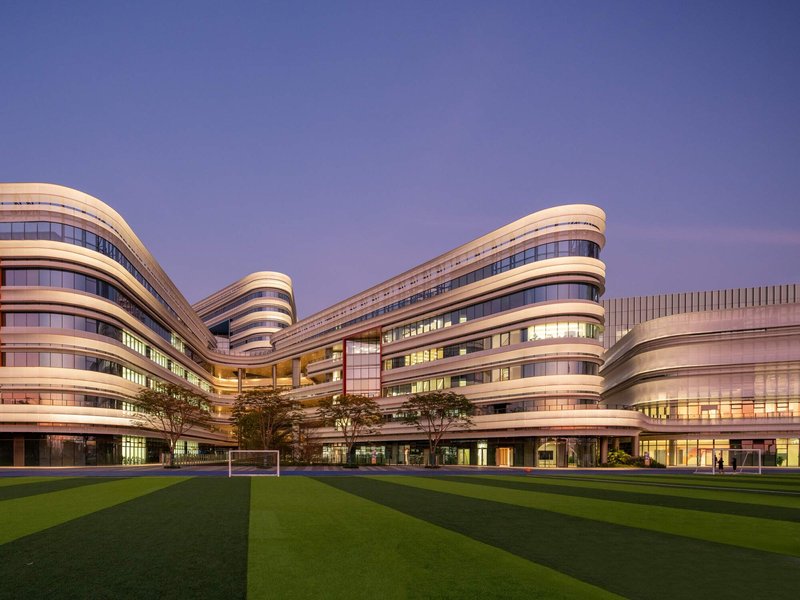Campus courtyard view showing interconnected horizontal facade bands and playing field at twilight