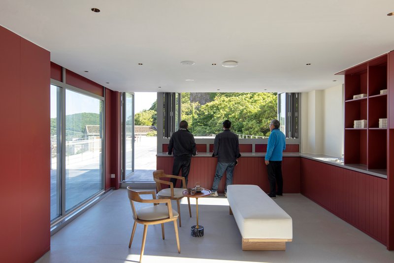 Living room with red built-in millwork and three people looking out toward treetops in daylight