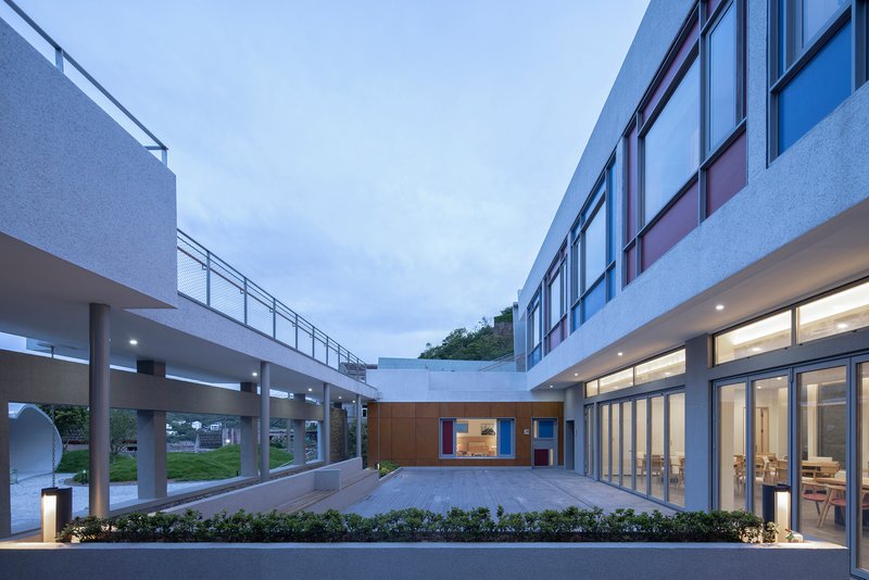 Enclosed courtyard flanked by elevated walkways and glazed volumes under a twilight sky