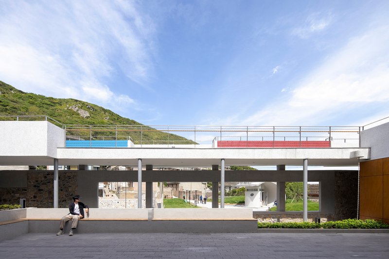Elevated concrete platform on columns with colored panels and two people seated below