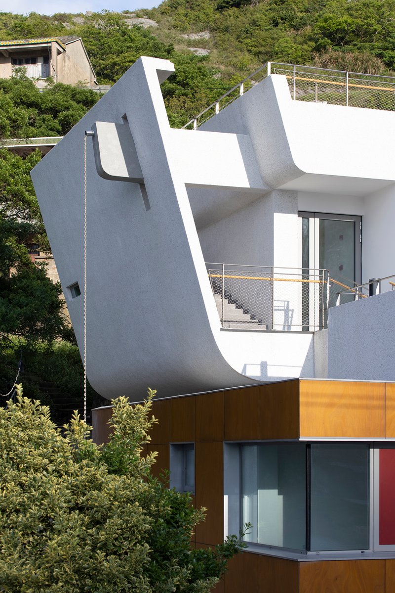 Angled white facade with metal railings and mustard-colored lower volume set against dense hillside vegetation