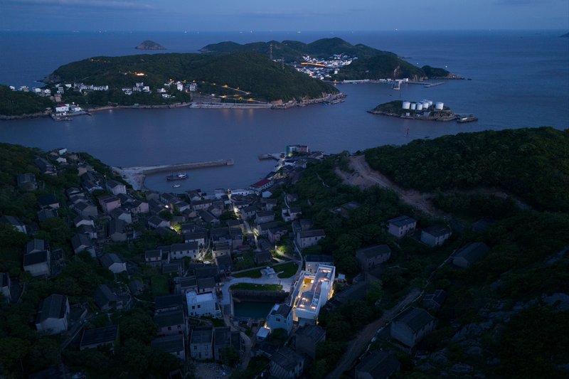 Drone view of illuminated rooftop among coastal village buildings at twilight