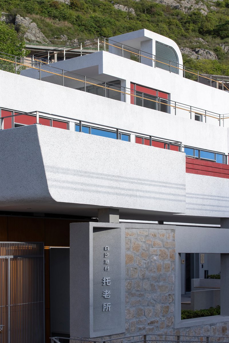 Entry gate with stone wall and signage below white terraced levels with colored window panels