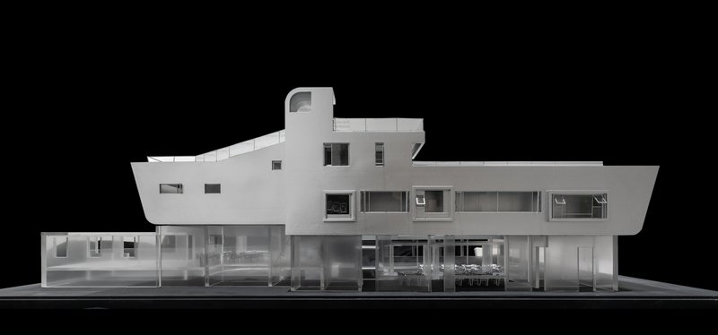 Physical model elevation showing a white two-story facade with horizontal ribbon windows and transparent ground floor