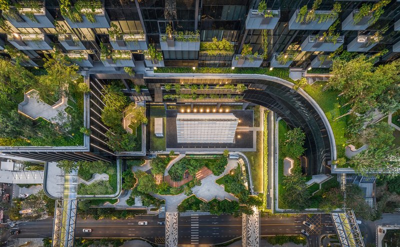 Aerial view of curved vehicular drive threading through planted roof terraces at dusk with lights on