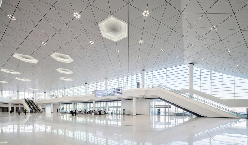 Interior departure hall with white polished floor, triangular ceiling panels and hexagonal skylights