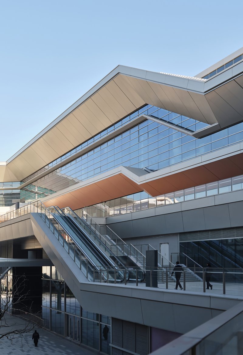 Stacked horizontal volumes with glazed facades and outdoor escalators carrying passengers between levels