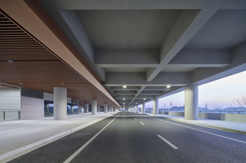 Covered roadway with concrete beams and cylindrical columns framing an open horizon at dusk