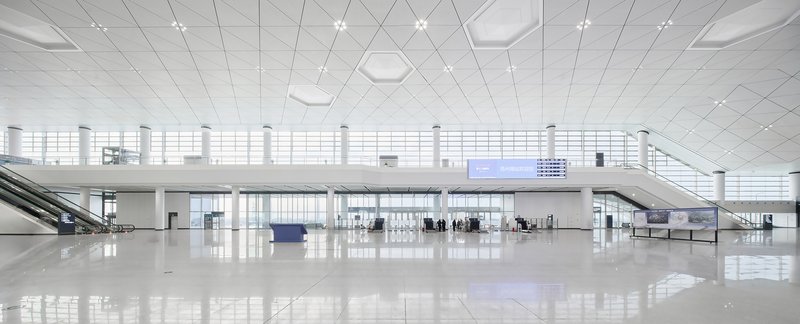 Interior departure hall with white tile ceiling, mezzanine level and passengers near service counters