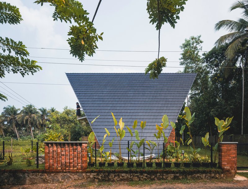 Side view of the tilted gable roof and perforated brick screen walls with young banana plants along the fence