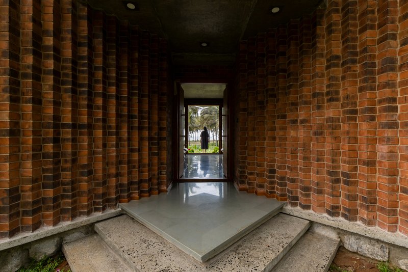 Covered entry corridor with perforated brick walls and polished concrete floor looking toward glazed doorway and garden