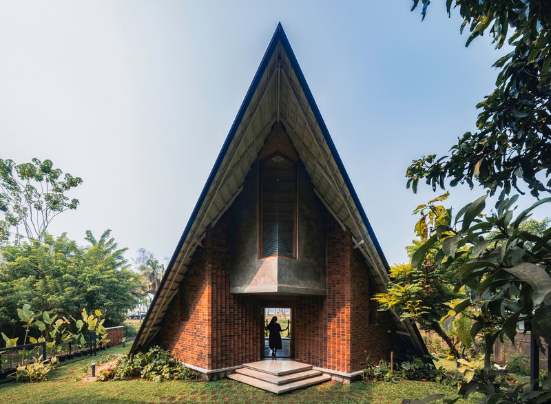 Frontal view of the triangular brick pavilion with steep roof and central entry door