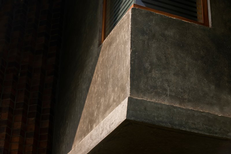 Concrete beam edge and window opening catching raking light across the textured plaster surface