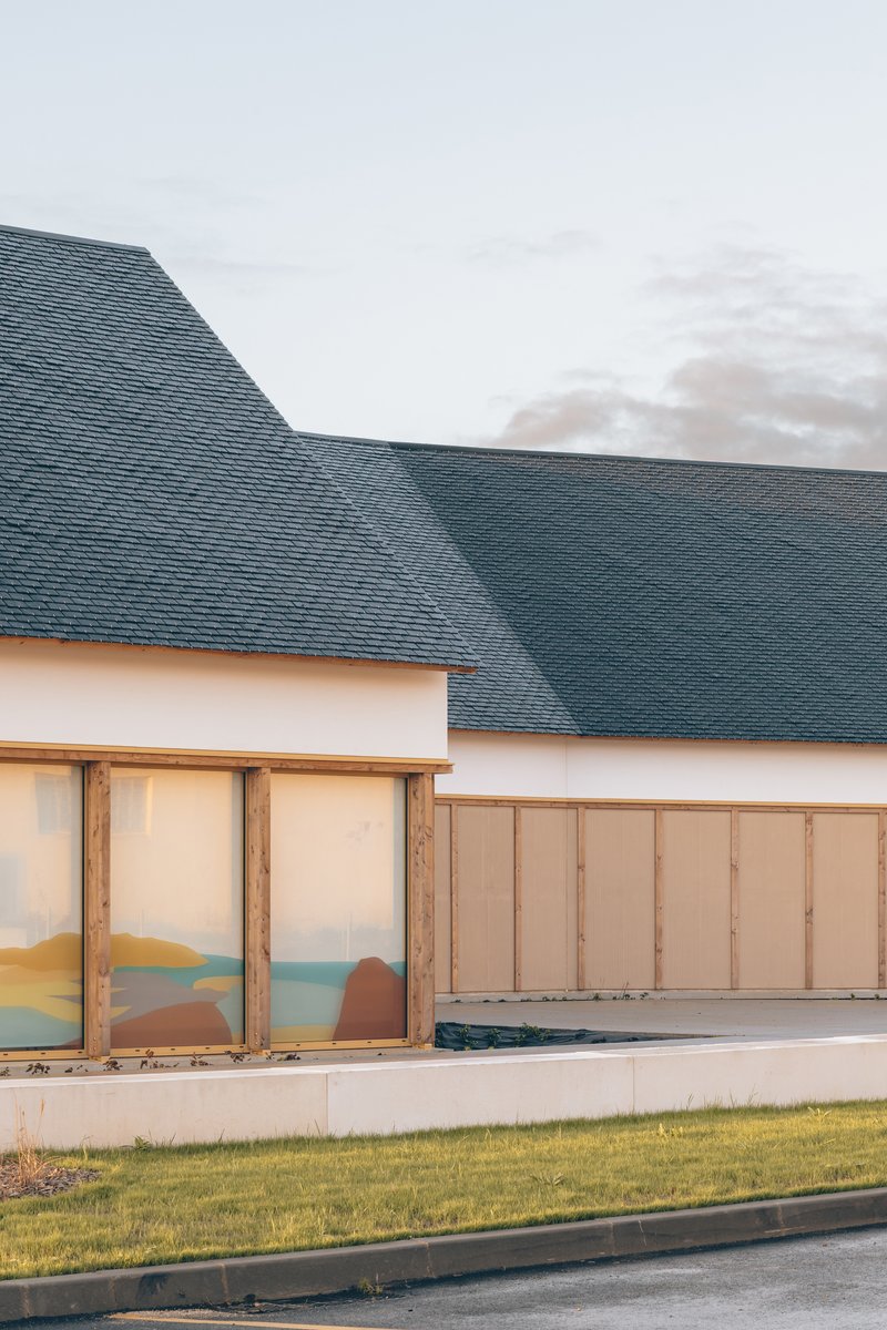 Detail of the dark slate roof meeting white walls and timber-framed glazing with lawn in foreground