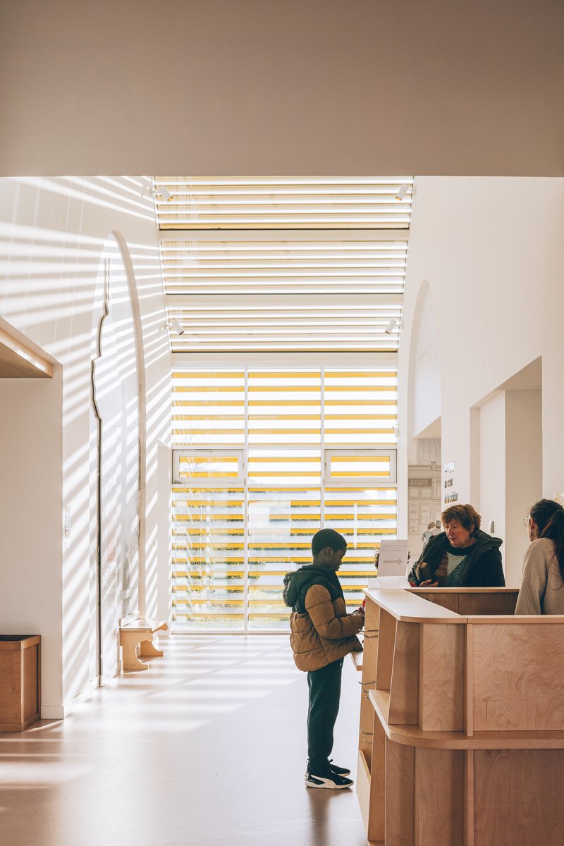 Reception desk with timber screen casting striped shadows across visitors in the entry hall