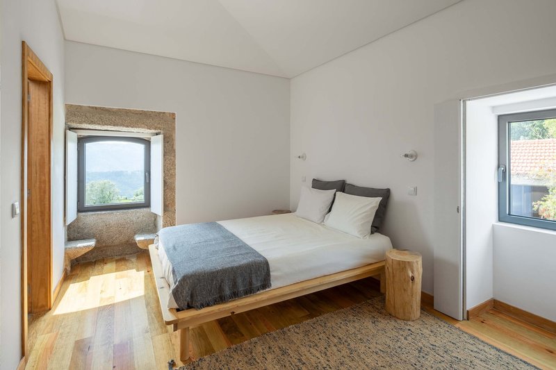 Bedroom with timber platform bed and cork-lined window nook overlooking distant landscape