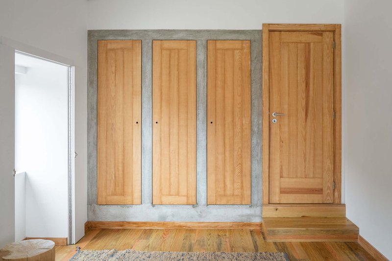 Built-in wardrobe with three timber doors framed by raw concrete on a timber floor
