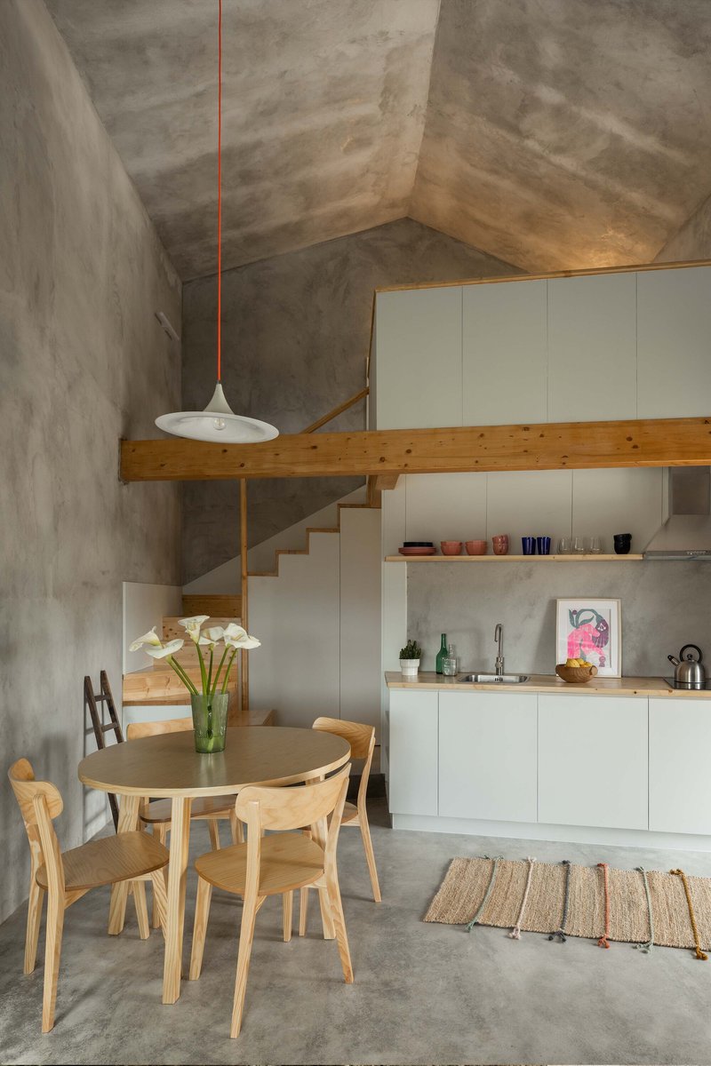 Double-height kitchen and dining area with raw concrete walls and timber mezzanine overhead