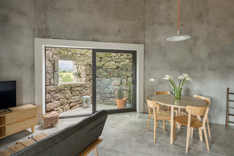 Polished concrete floor and dining table framed by glazed opening revealing the stone wall courtyard beyond