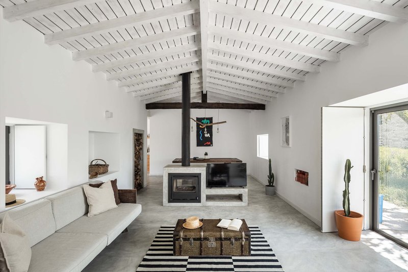 Living room with white painted timber ceiling, exposed dark beams and a concrete masonry fireplace