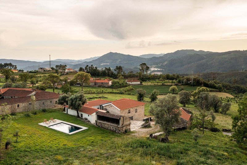 Renovated stone farmhouse complex with red tile roofs and swimming pool in hilly landscape at dusk
