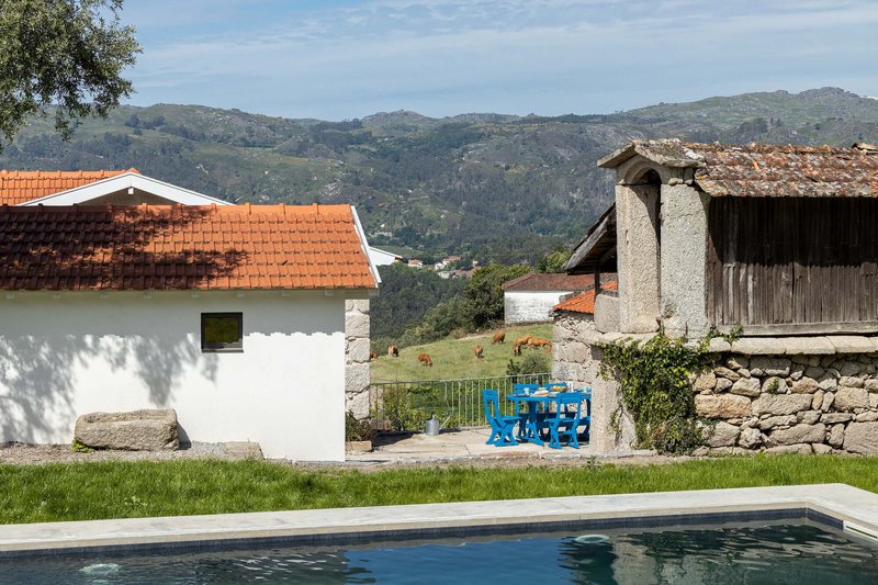 Swimming pool edge with white plastered volume and blue painted furniture against mountain backdrop