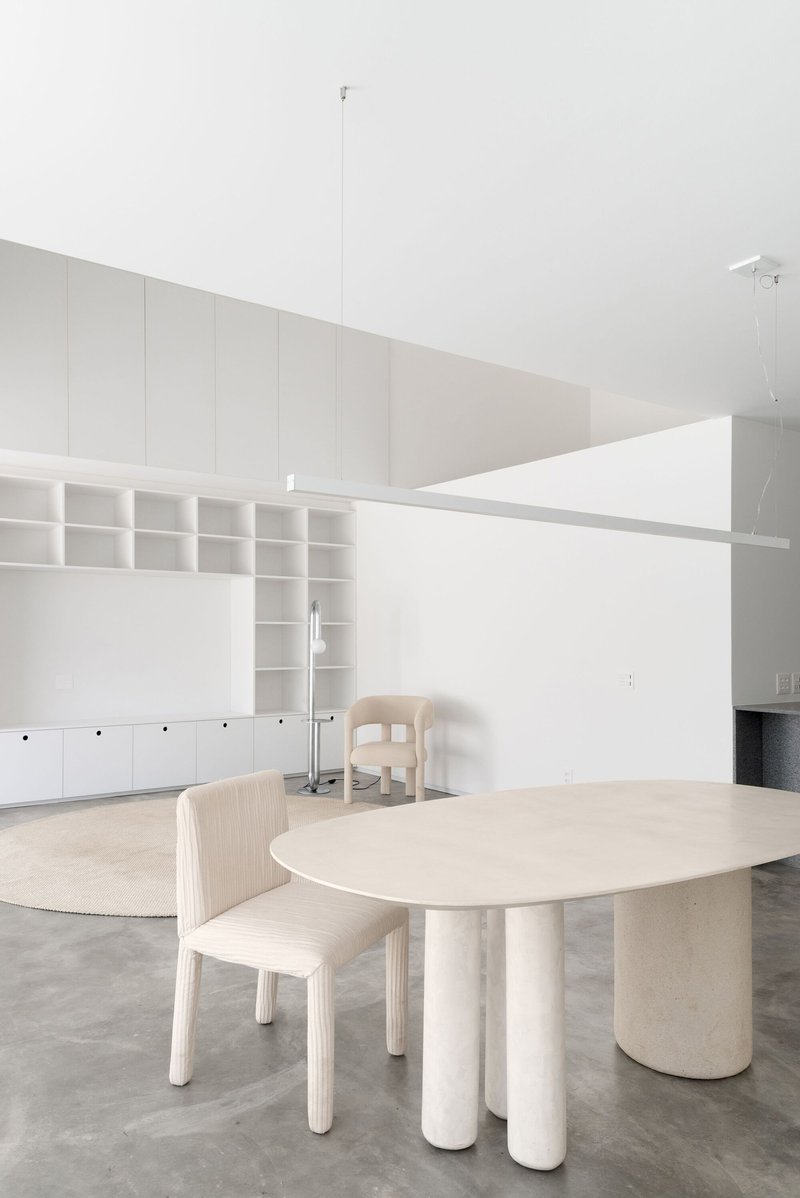 Dining area with pale wood table on cylindrical legs and built-in shelving beneath a sloped ceiling
