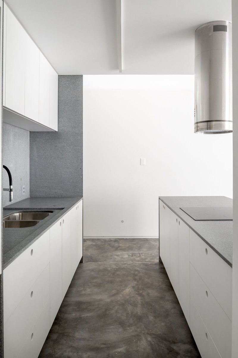 Galley kitchen with white cabinetry, grey terrazzo countertops and a cylindrical stainless steel range hood