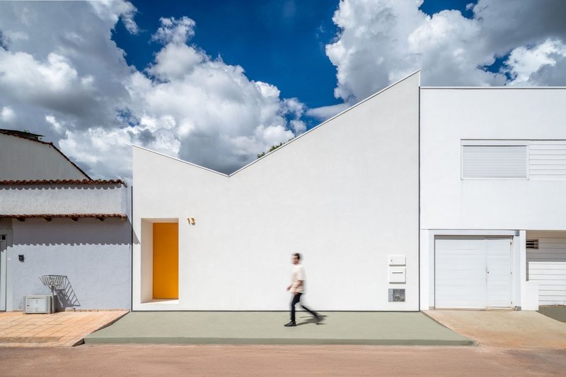 White stucco facade with recessed orange doorway and a person walking across the concrete entrance under blue sky