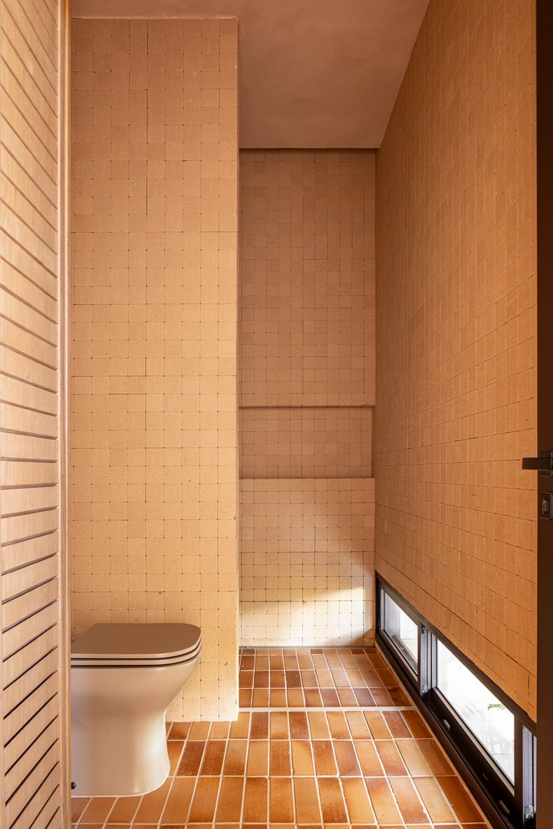 Tiled bathroom with timber wall panels and horizontal slit window at floor level