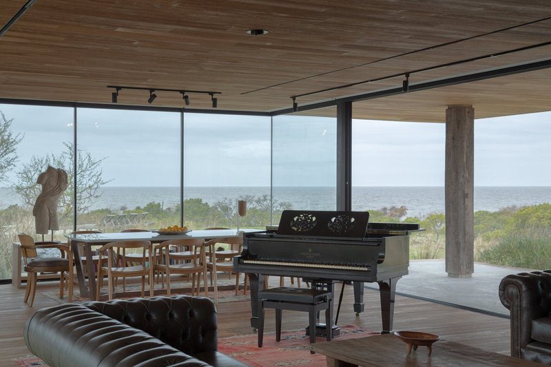 Dining and living area with glazed walls opening to the ocean horizon under diffused daylight