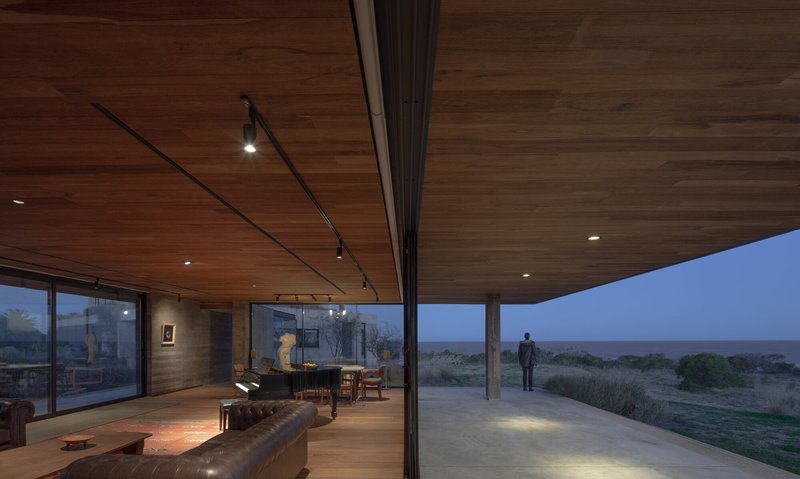 Interior terrace at dusk with timber ceiling, track lighting, and a figure silhouetted against the landscape