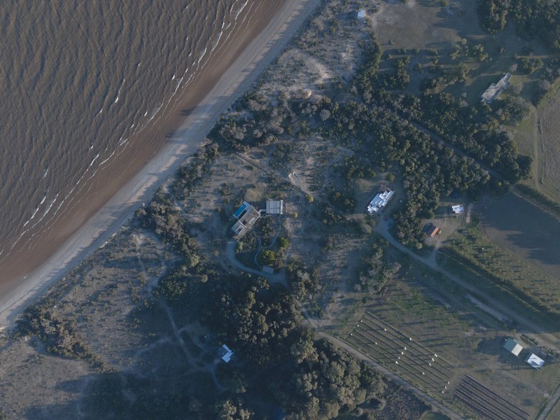 Aerial view of clustered buildings among trees between beach and cultivated fields