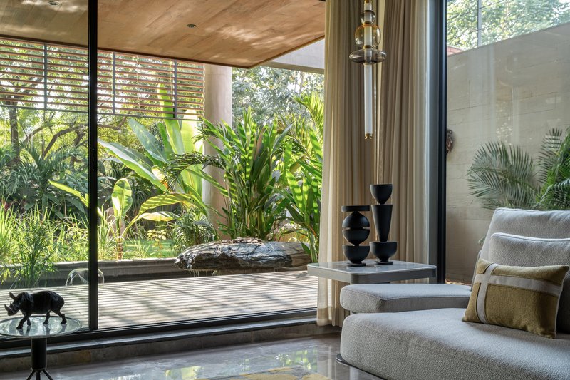 Interior living space opening to timber deck, water feature and lush garden through floor-to-ceiling glazing