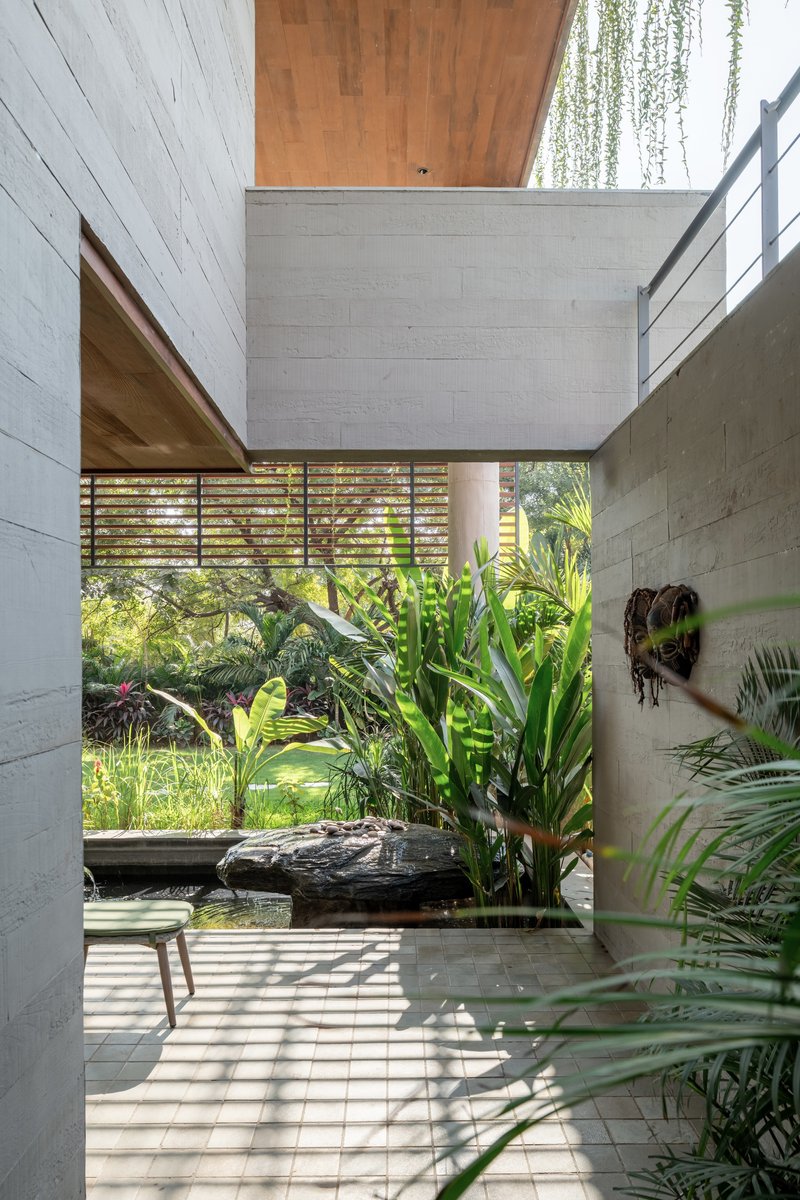 Narrow courtyard passage with board-formed concrete walls, timber ceiling soffit and planted reflecting pool
