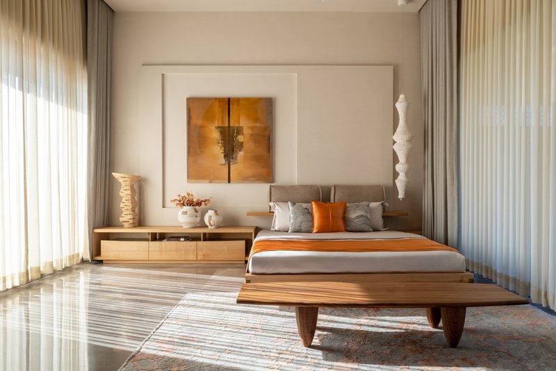 Bedroom with low timber platform bed and sheer curtains filtering daylight across glossy floor