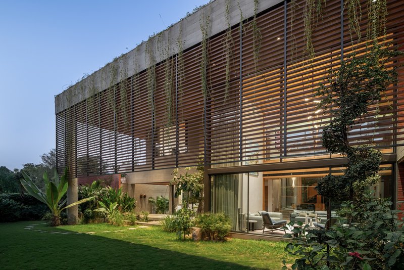 Garden facade at dusk showing illuminated interior behind glass and horizontal timber louvers with cascading plants