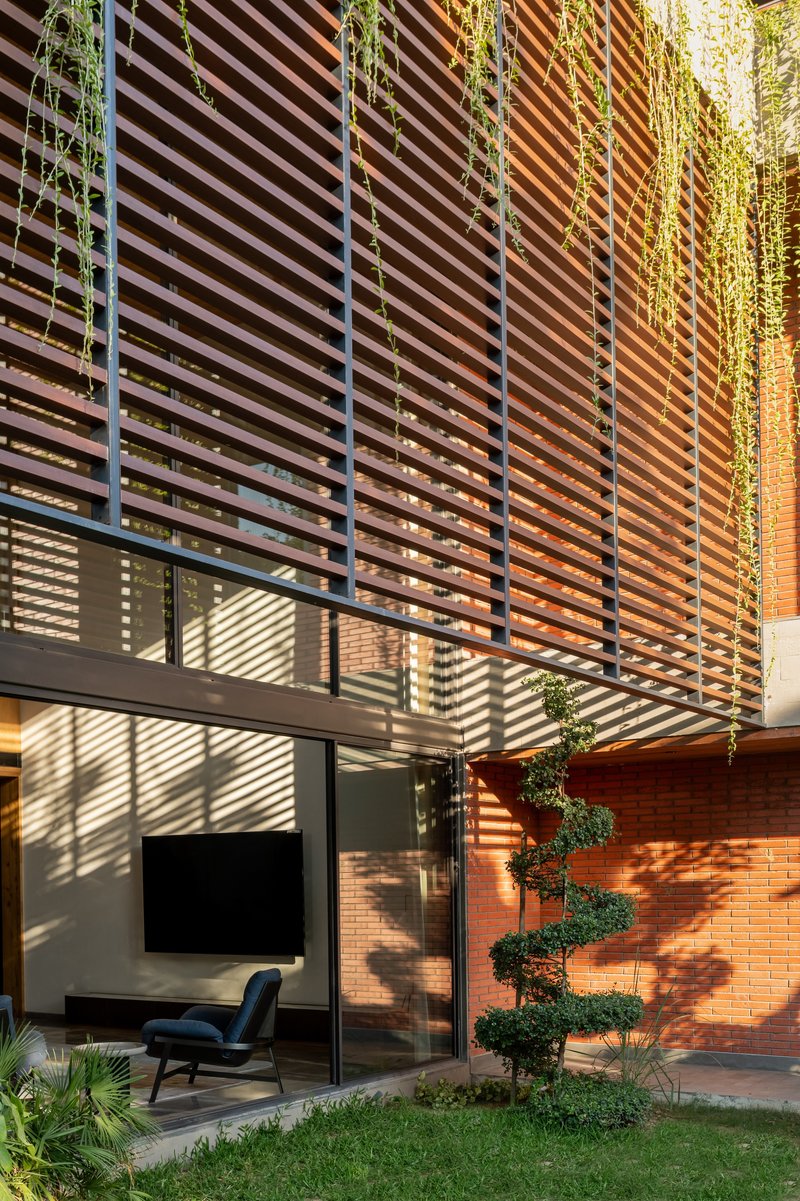 Timber louvers casting striped shadows on a courtyard wall with a spiral topiary and red brick
