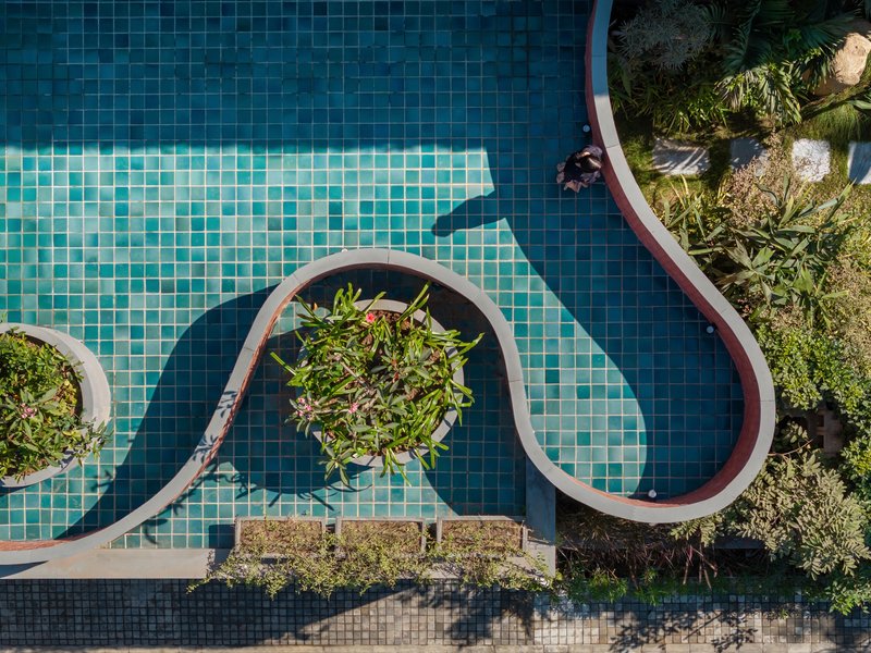 Aerial view of the turquoise mosaic tile pool with curving brick planters and tropical vegetation