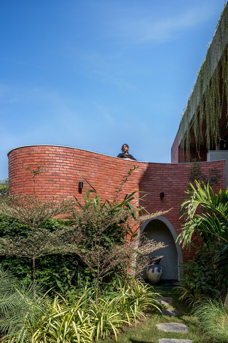 Curved red brick wall with an arched opening and a figure standing on the upper edge