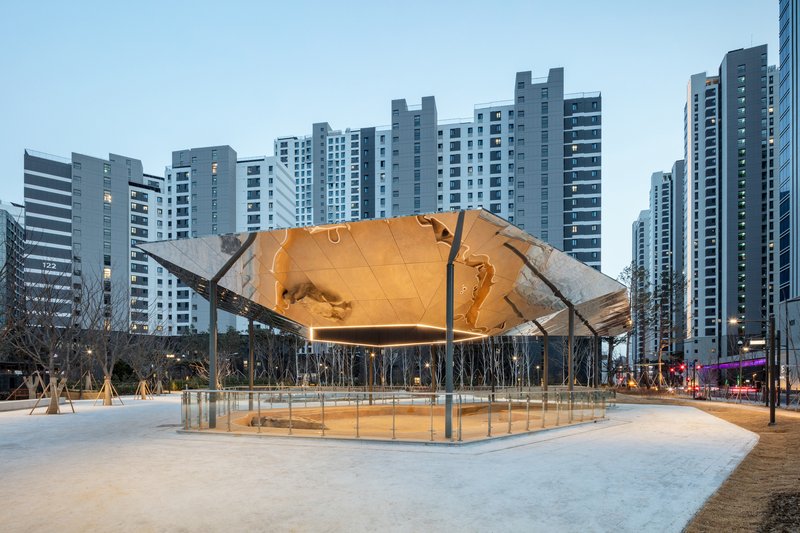 Elevated hexagonal canopy with illuminated copper-toned underside above a glass-enclosed plaza at dusk